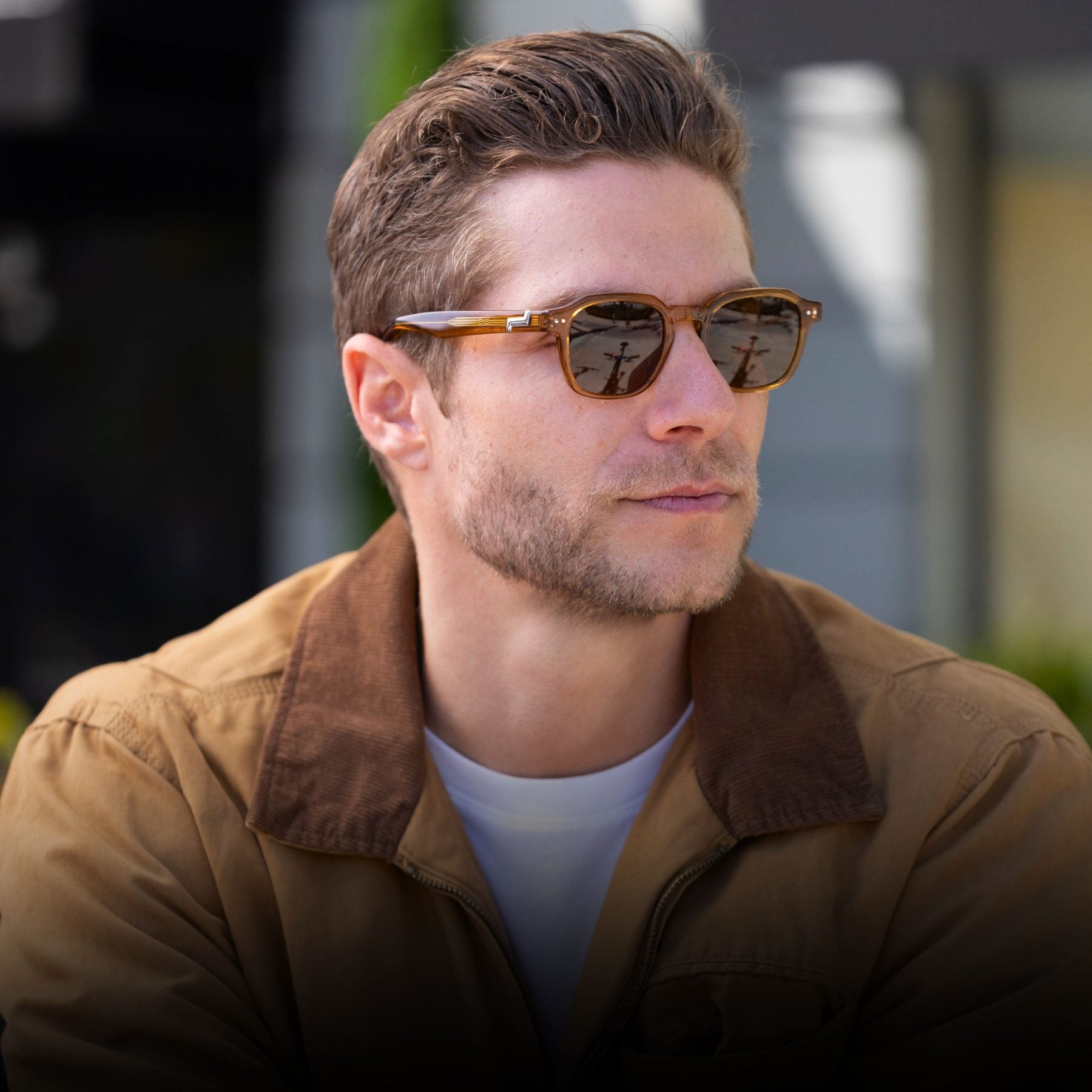 Man in a tan jacket wearing honey-amber KIAURA sunglasses in sunlight.